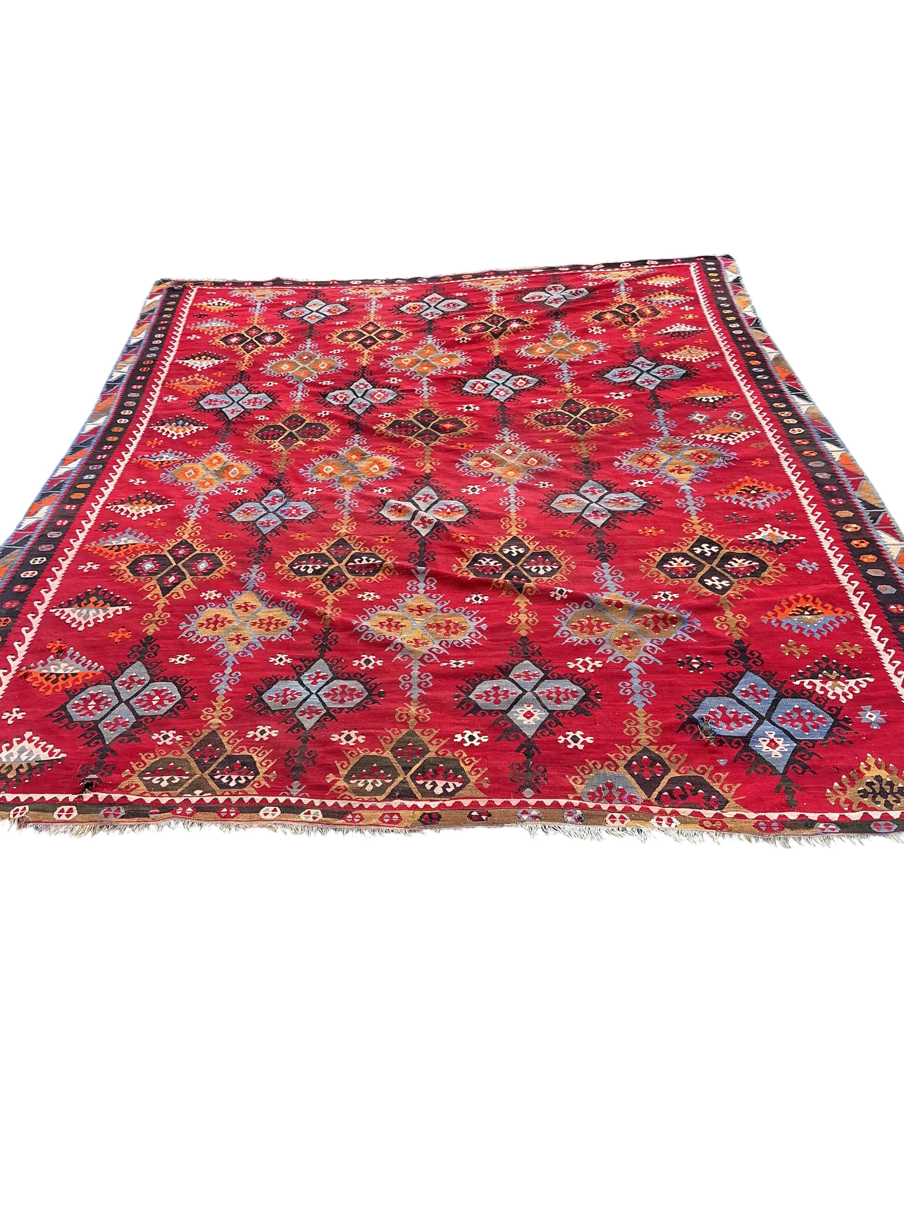 A Turkish Anatolian polychrome flatweave Kilim carpet, woven with geometric lozenges on a red field, 367 x 292cm